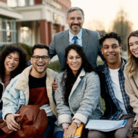 Portrait of happy university students and their teacher outdoors at campus. They are looking at camera.